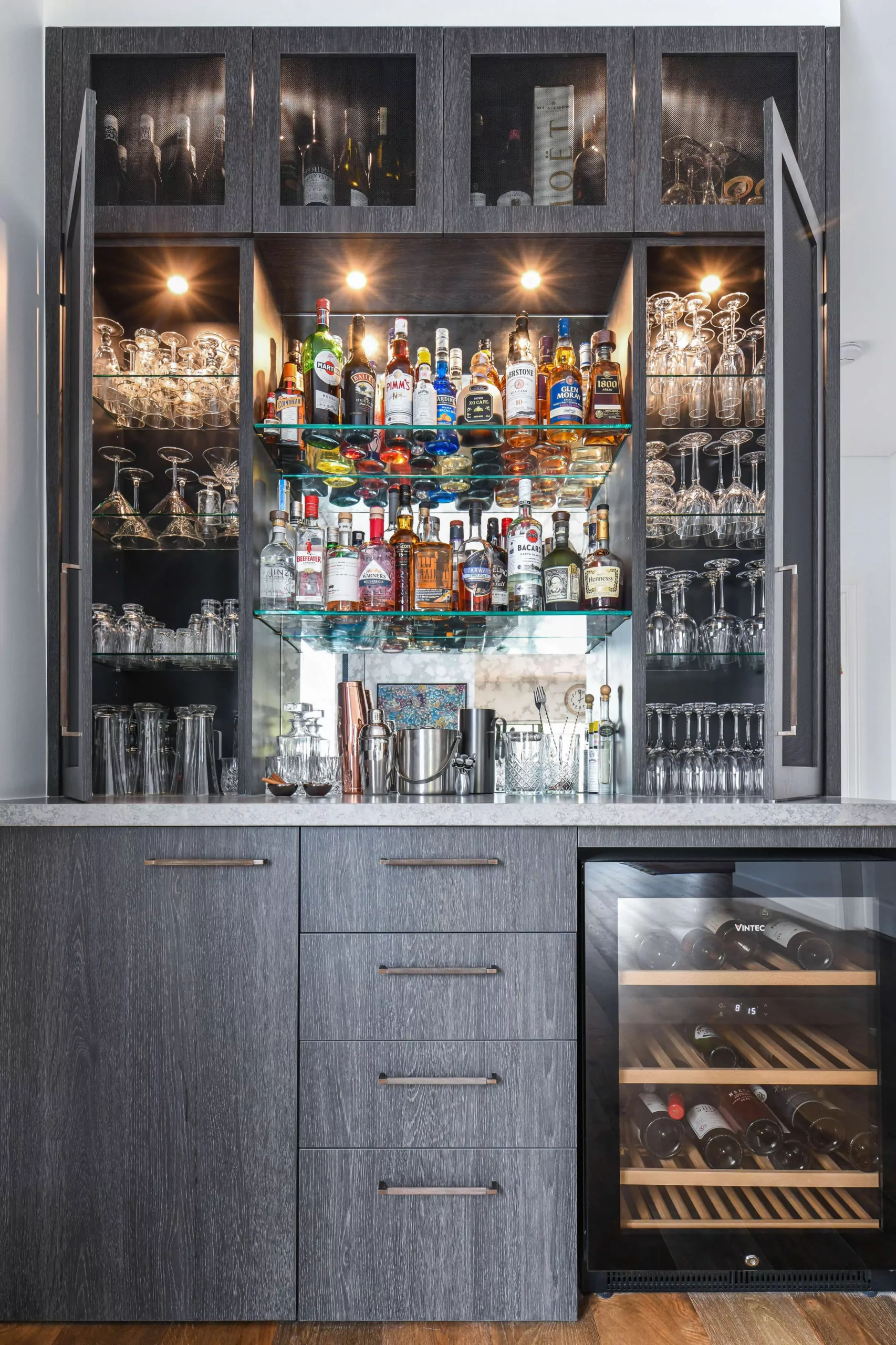 Home bar with backlit glass shelving, wire mesh cabinets, and wine fridge | Custom joinery by Improva, Kingsford